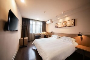 Habitación de hotel con una cama grande, un escritorio, una silla, un televisor de pantalla plana montado en la pared y una ventana con cortinas.