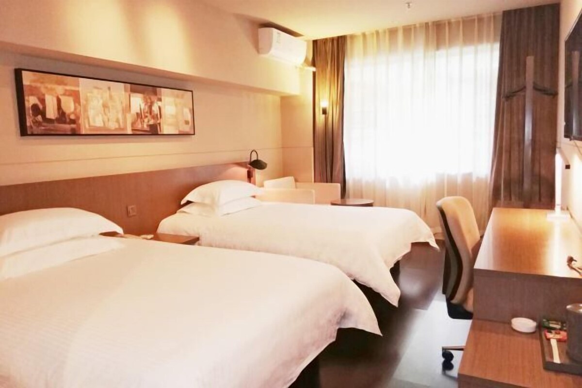 Habitación de hotel con dos camas, un escritorio, una silla, una lámpara y una ventana con cortinas.