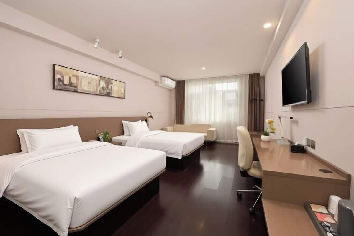 A hotel room with two beds, a desk, a chair, a TV, and a painting on the wall.