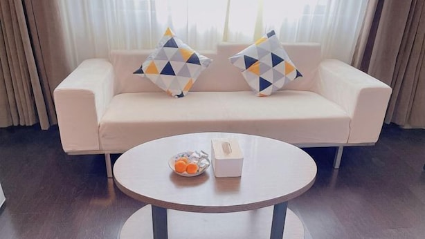 A modern living room with a white sofa, two geometric-patterned pillows, a round wooden coffee table with a tissue box and a bowl of fruit. - Jinjiang Inn Style (Huaxi District Xiahe Vanke Metropolis Store GuiyangGuizhou) (Guiyang)