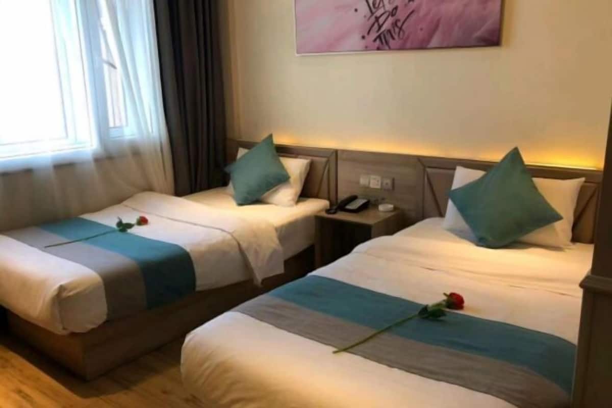 Quarto de hotel com duas camas, cada uma com uma almofada azul-turquesa e uma rosa na colcha.
