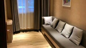 A room with a grey sofa, a small table, and a window with curtains.