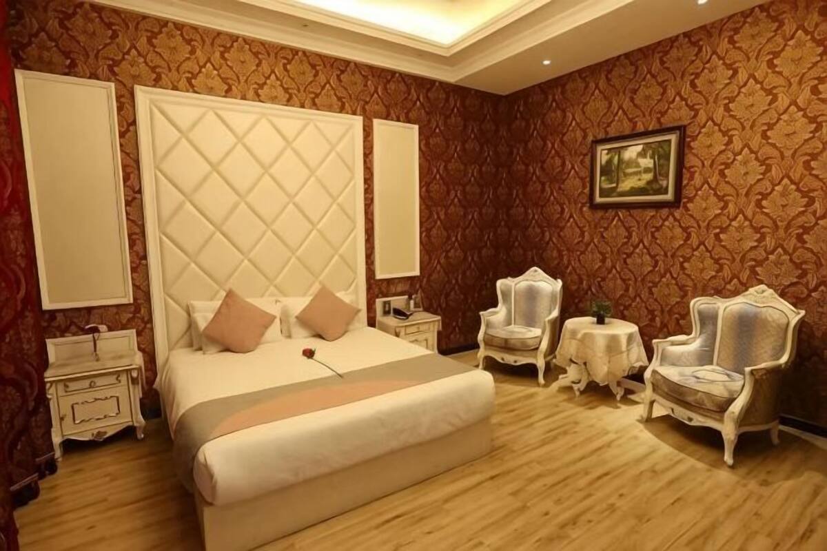 Quarto com uma cama grande, duas mesas de cabeceira, uma cadeira, uma pequena mesa e um quadro na parede.
