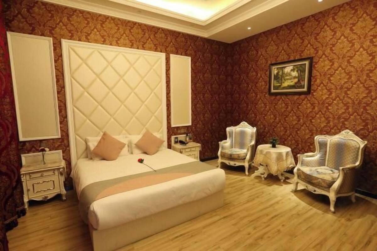 Quarto com cama grande, duas mesas de cabeceira, duas cadeiras e uma pequena mesa.