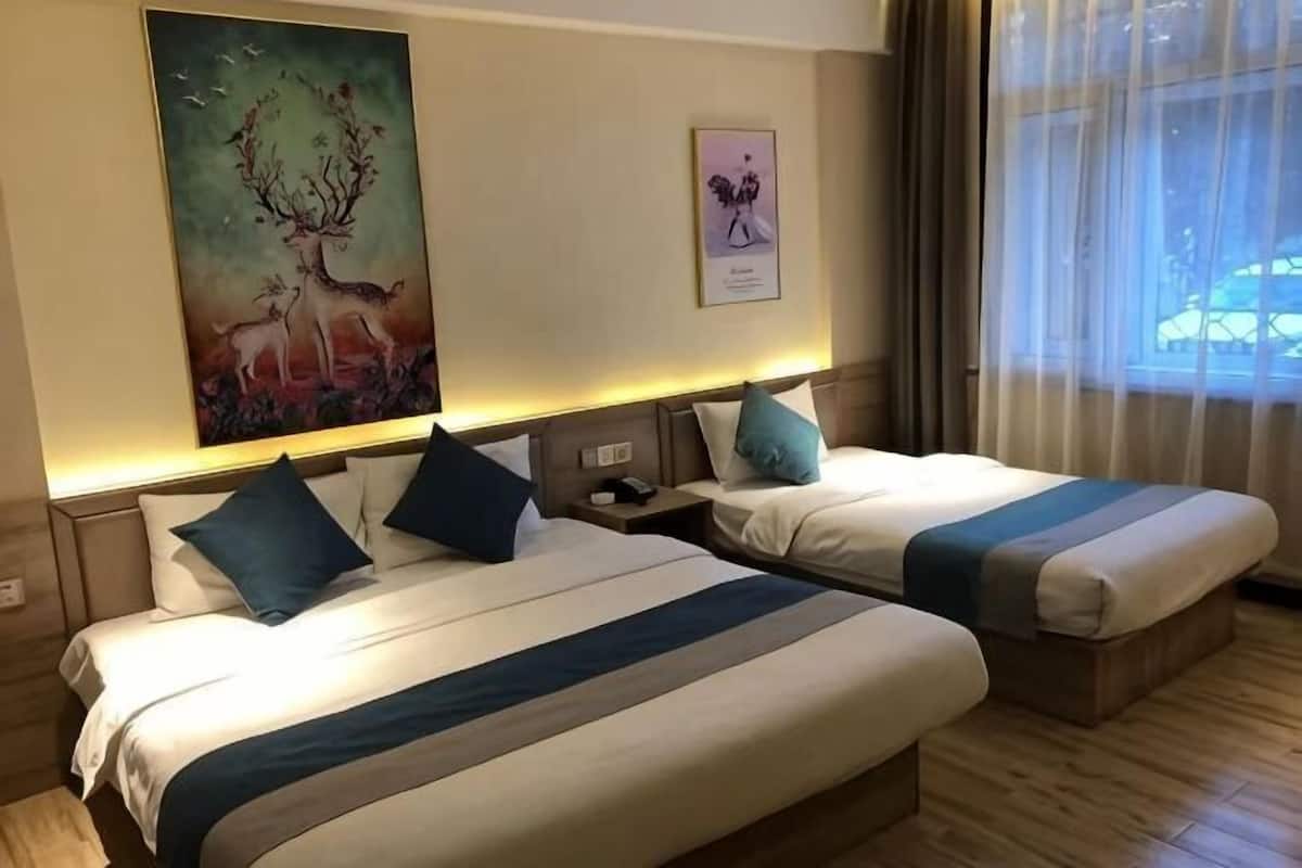 Quarto de hotel com duas camas, uma mesa de cabeceira, um quadro e uma janela com cortinas.