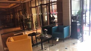 A lobby with a yellow armchair, a blue sofa, and a small table with a vase.