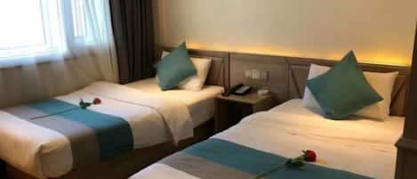 A hotel room with two beds, each with a blue and white striped bedspread, a single rose on each bed, and a nightstand with a phone.