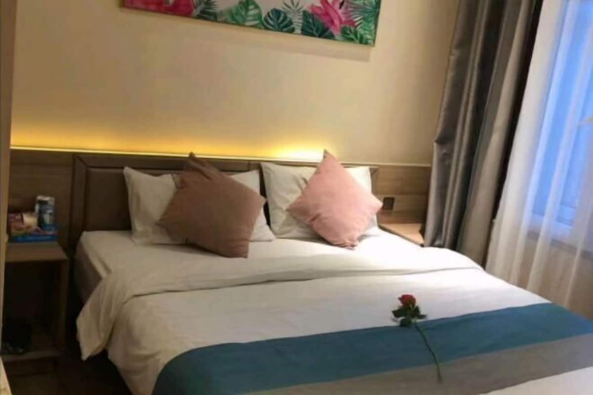 Quarto de hotel com cama, almofadas, mesa de cabeceira, um quadro na parede e uma janela com cortinas.