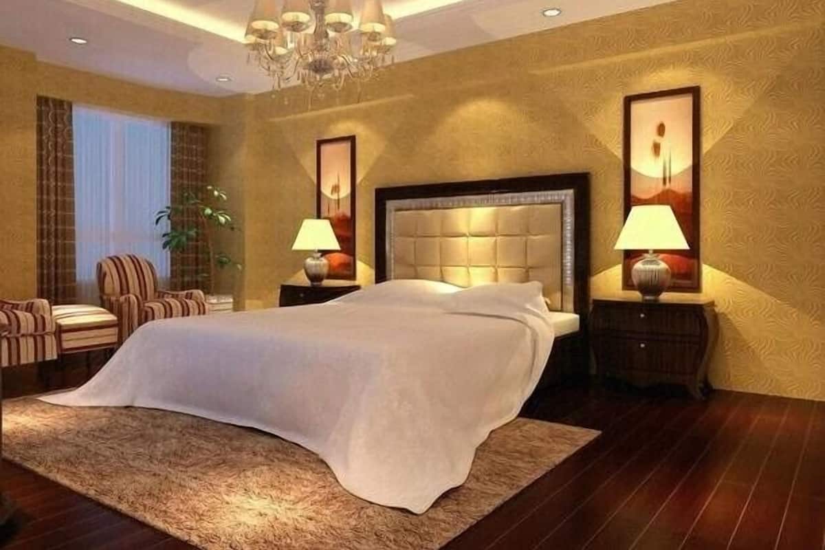 Une chambre spacieuse avec un grand lit, un lustre, deux tables de chevet avec des lampes, une plante en pot et une vue sur l’extérieur par une fenêtre.