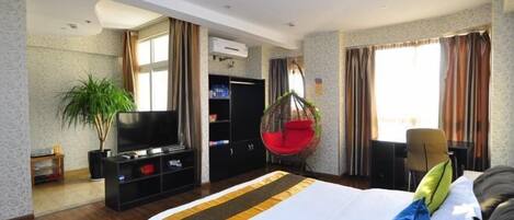 A hotel room with a large bed, a TV, a plant, and a red hanging chair.