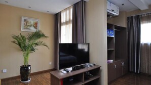 Een woonkamer met een flatscreen televisie, een kamerplant en een boekenplank.