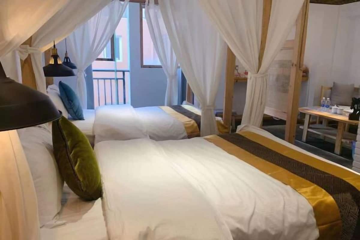 Une chambre d’hôtel avec deux lits, du linge de lit blanc, un lit à baldaquin, une petite table et une vue sur l’extérieur.