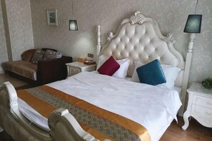 A hotel room with a large bed, a bedside table, a nightstand, a lamp, and a sofa.