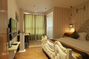 A hotel room with a bed, a TV, a desk, and a window with curtains.