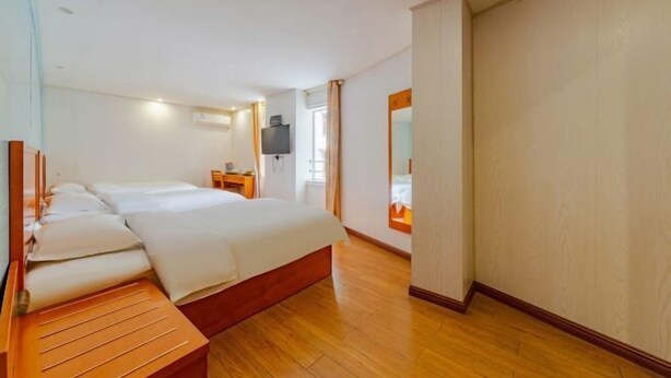 Habitación de hotel con una cama grande, un banco de madera, un escritorio con silla, un televisor de pantalla plana y un espejo grande.