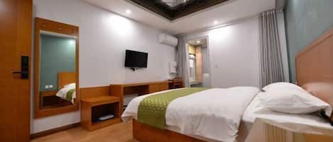 A hotel room with a bed, a TV, a mirror, and a skylight.