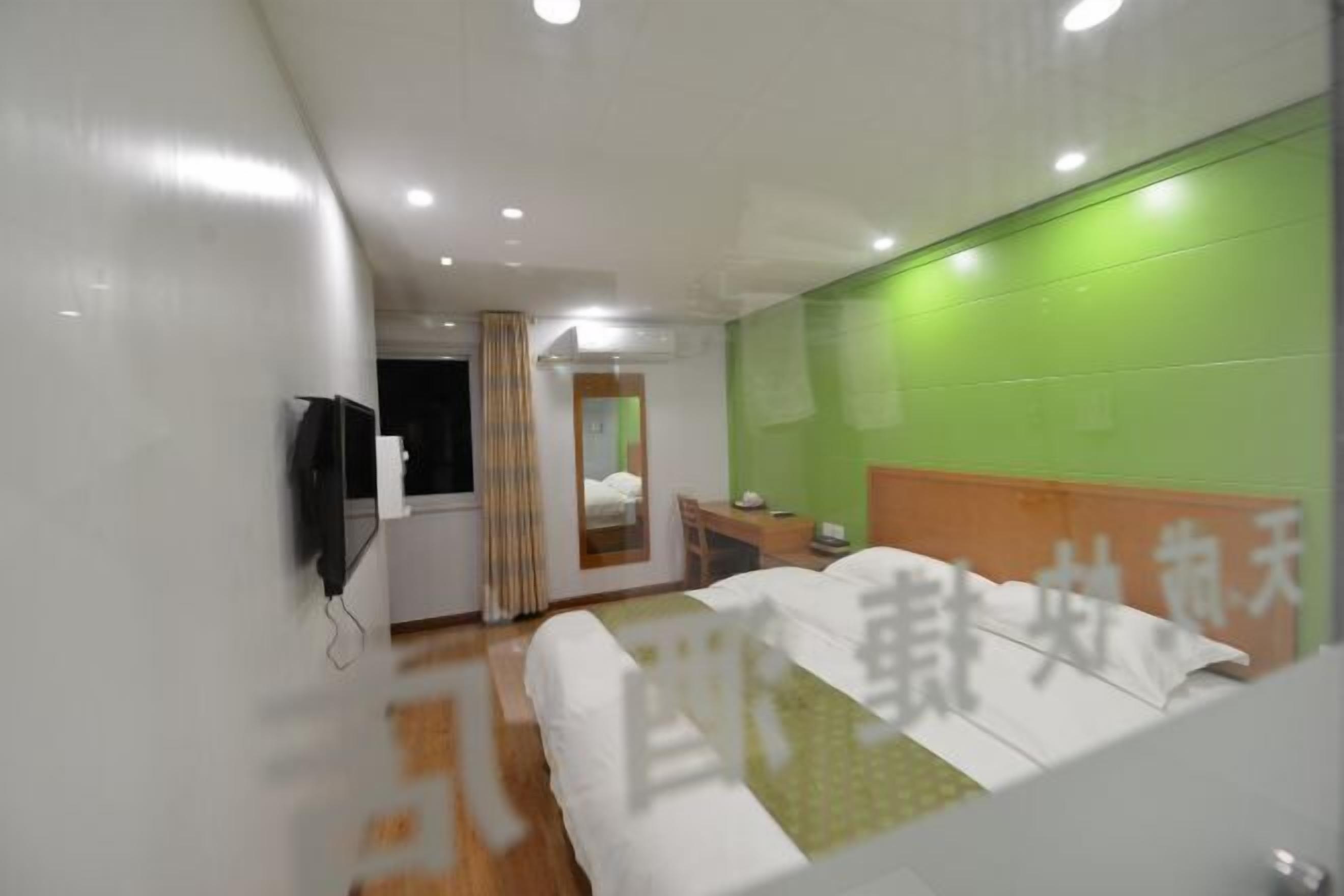 A hotel room with a bed, a desk, a chair, a television, and a green accent wall.