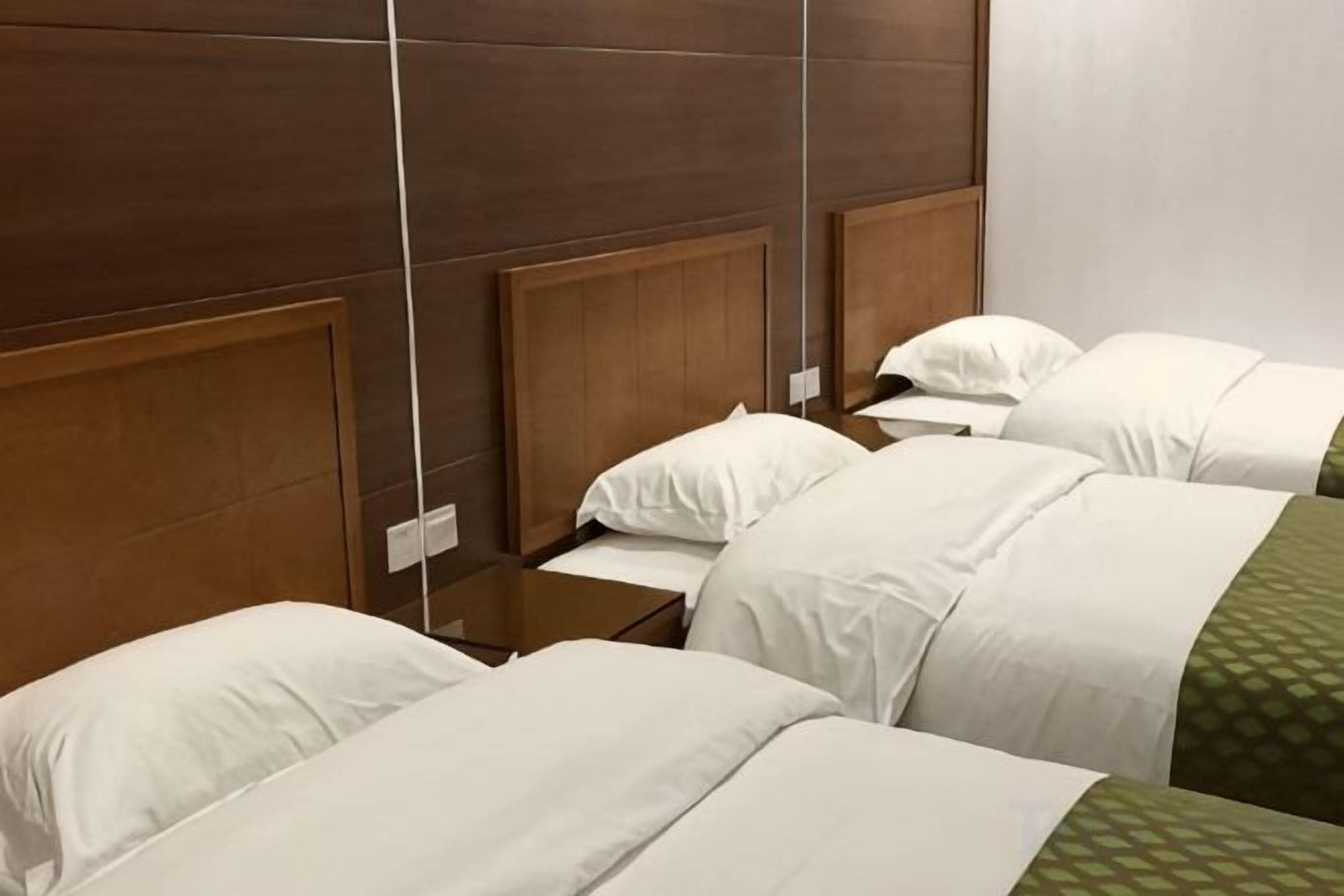 Habitación de hotel con cuatro camas individuales, cada una con cabecero de madera y ropa de cama blanca.