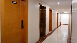 Un pasillo de hotel con puertas de madera, un cartel con un número y un ascensor.
