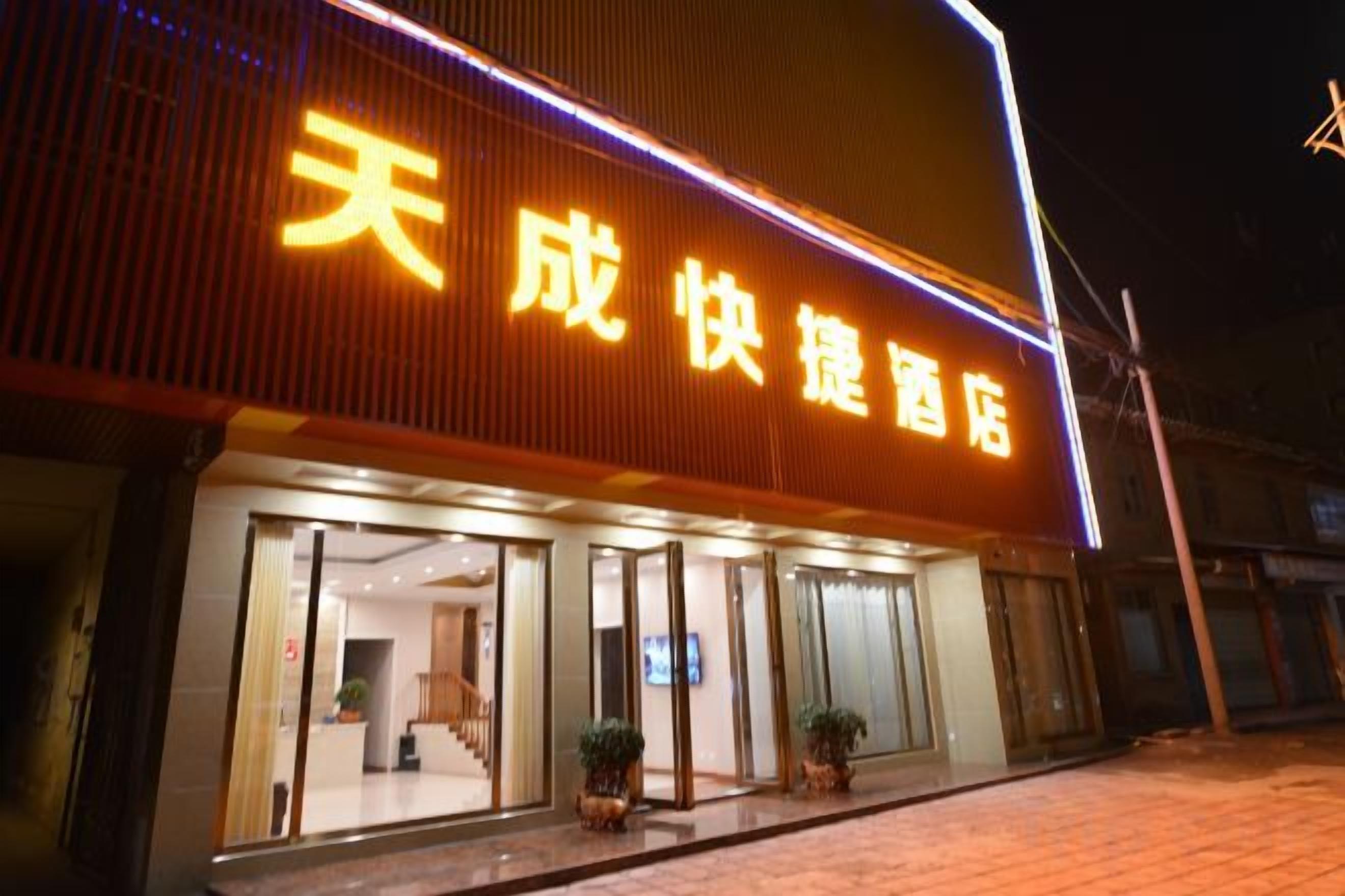 A hotel with a large illuminated sign, a glass entrance, and potted plants outside.