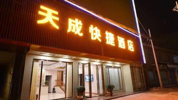 A hotel with a large illuminated sign, a glass entrance, and potted plants outside.