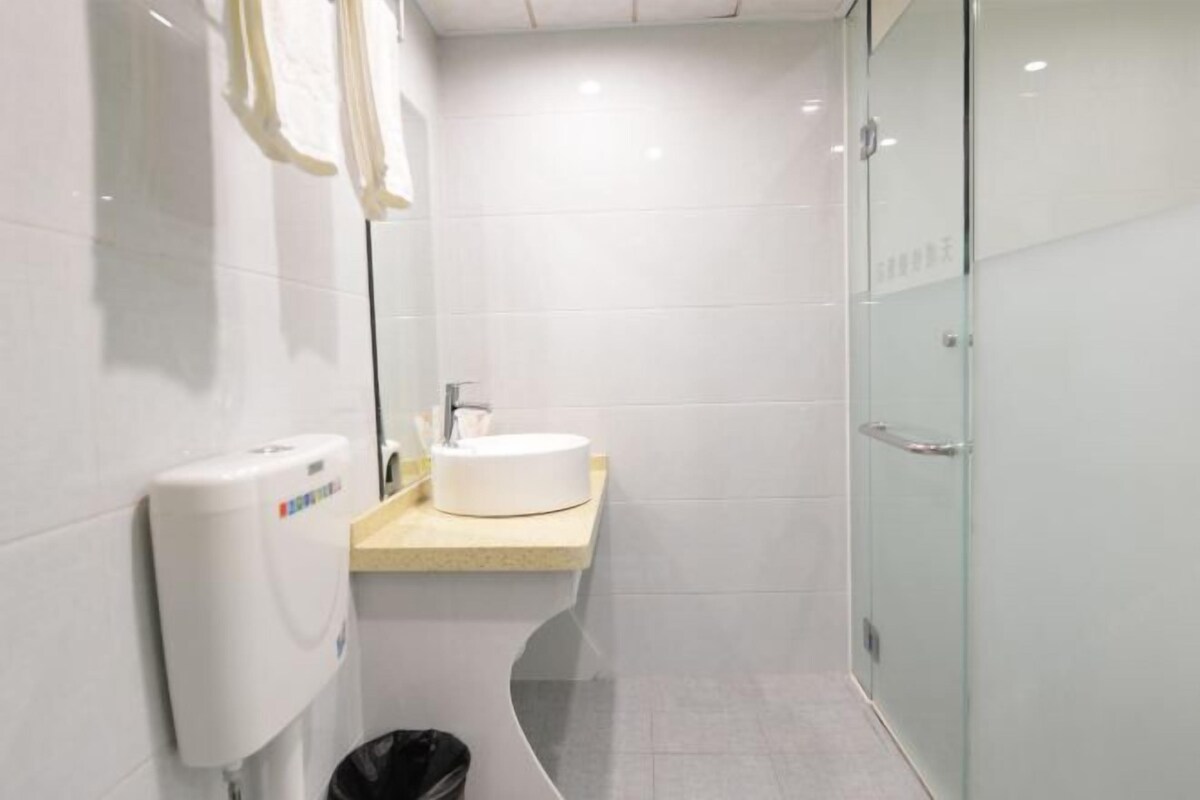 A modern bathroom with a white sink, a glass shower enclosure, and a hand sanitizer dispenser.
