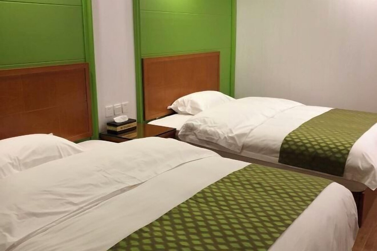 A hotel room with two beds, each with white bedding and a green patterned bedspread.