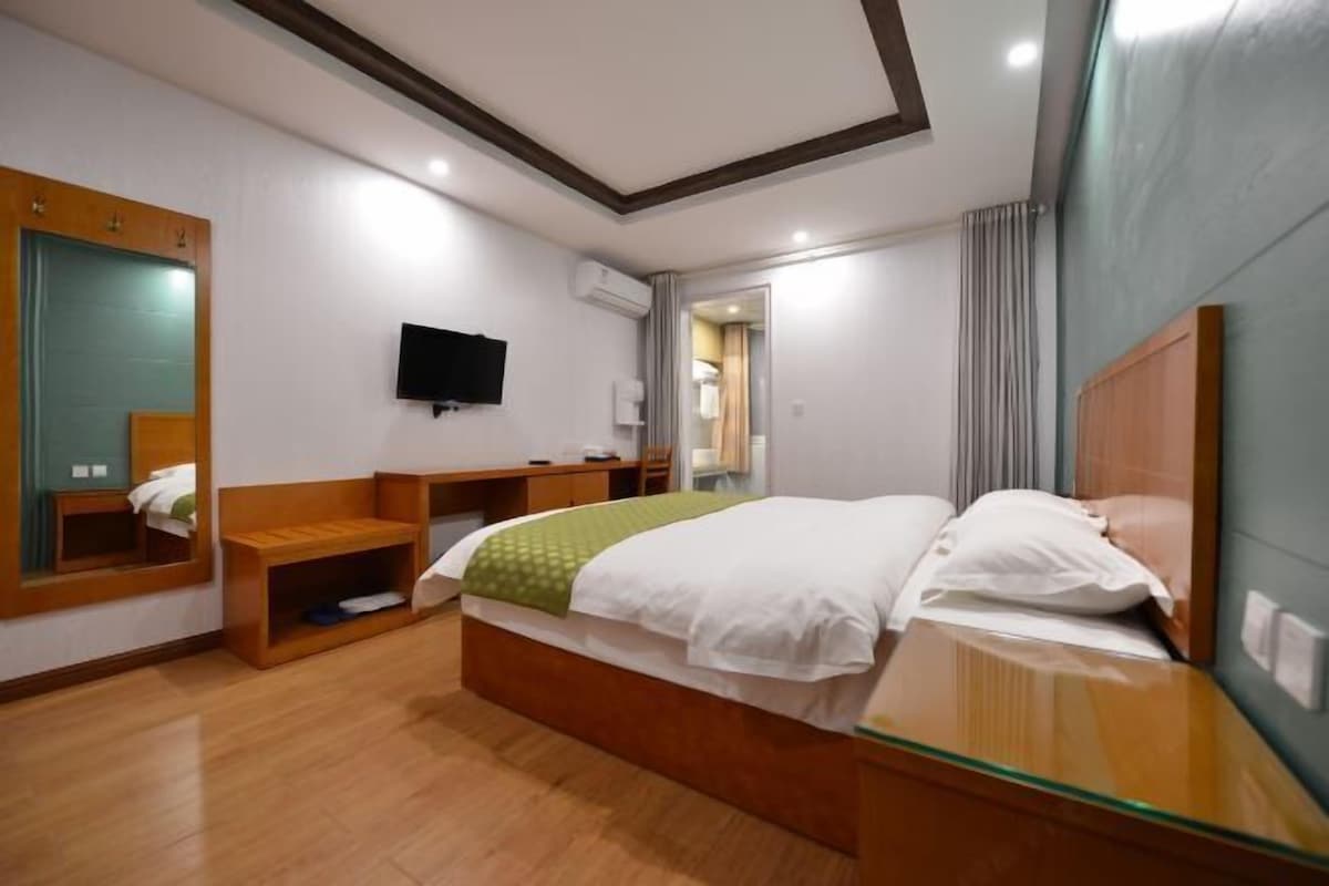 A hotel room with a wooden bed, a TV mounted on the wall, a desk, and a mirror.