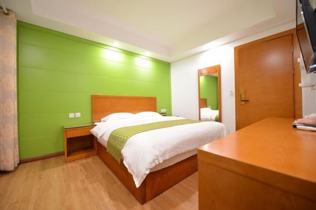 A hotel room with a bed, wooden headboard, green walls, a wooden nightstand, and a wooden dresser.