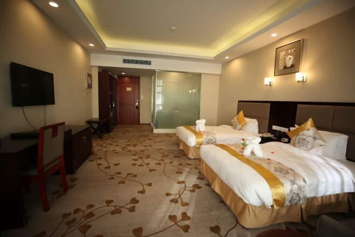 A hotel room with two beds, a desk, a TV, and a large window.