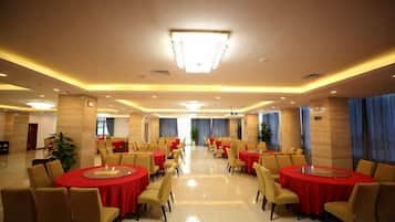 A spacious banquet hall with round tables and chairs, a chandelier, and a clean, polished floor.