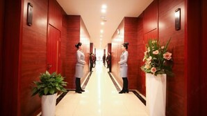 A hotel hallway with wooden walls, a central light fixture, and two receptionists standing at the end. - Sumahui Hotel (Suzhou East Railway Station Kechuang Center) (Suzhou)