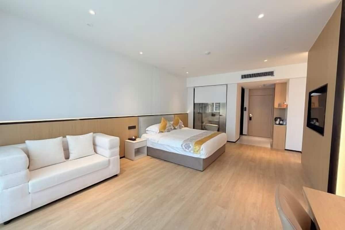 A modern hotel room with a bed, a sofa, a bedside table, and a mirror.