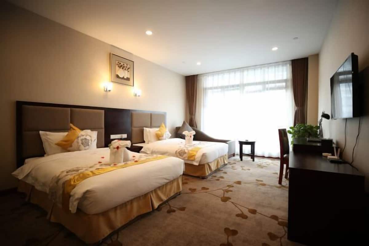 A hotel room with two beds, a desk, a chair, a TV, and a large window.