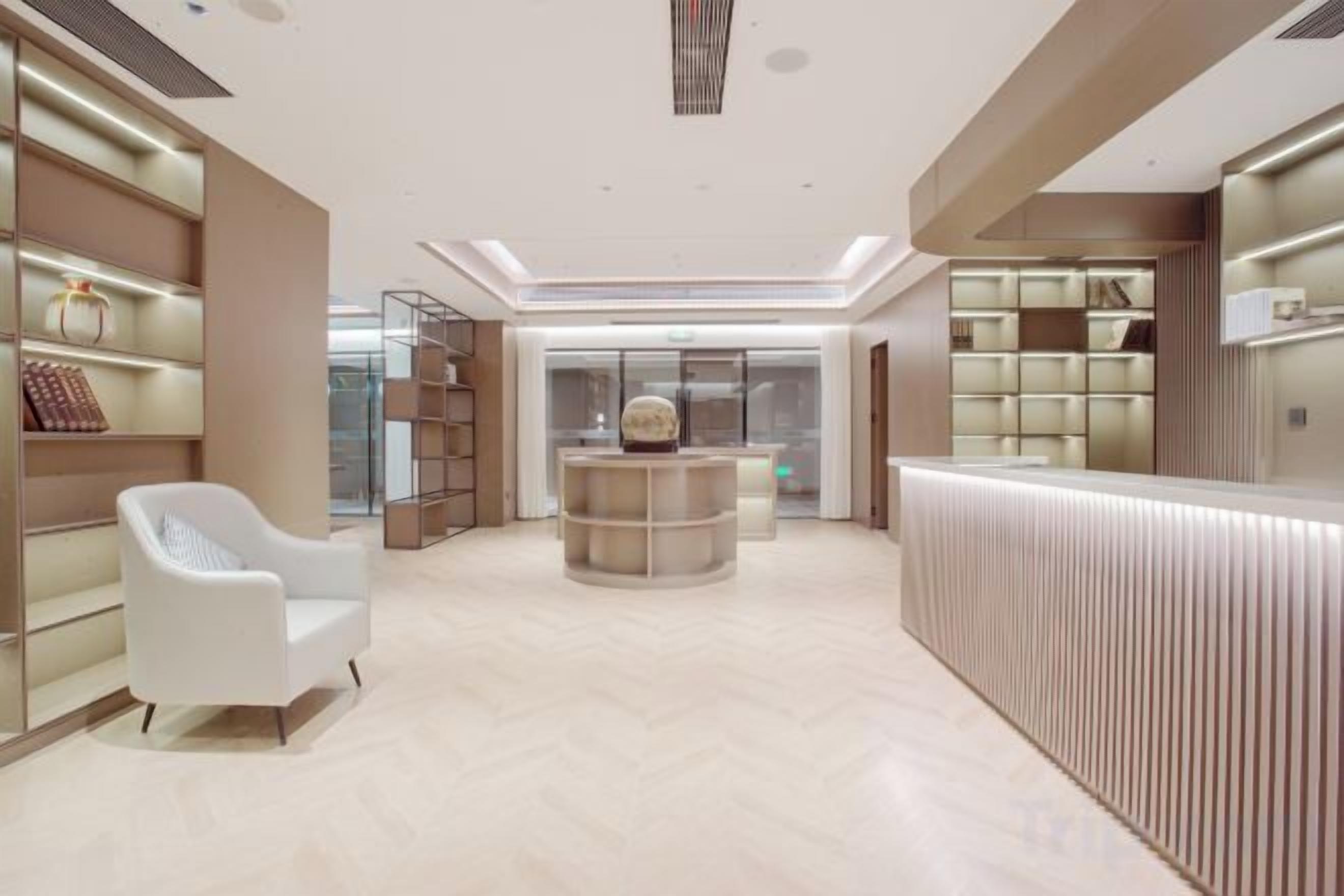 A modern hotel lobby with a reception desk, seating area, and shelving with items.