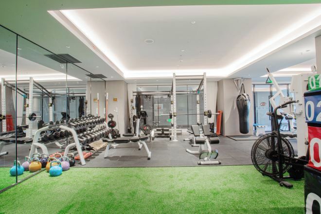 Ein Fitnessraum mit unterschiedlichen Trainingsgeräten, darunter Kurzhanteln, Kettlebells und ein Ergometer.