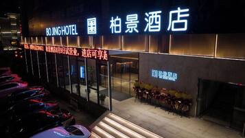 Ein Hotel Eingang mit leuchtendem Neonlicht, eine Treppe nach oben und eine Reihe geparkter Autos.