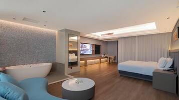 Ein modernes Hotelzimmer mit einer großen Badewanne, einem Sofa, einem runden Couchtisch, einem Bett und einem Schreibtisch.