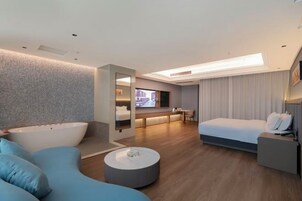Una habitación de hotel moderna con una bañera grande, un sofá, una mesa de centro redonda, una cama y un escritorio.