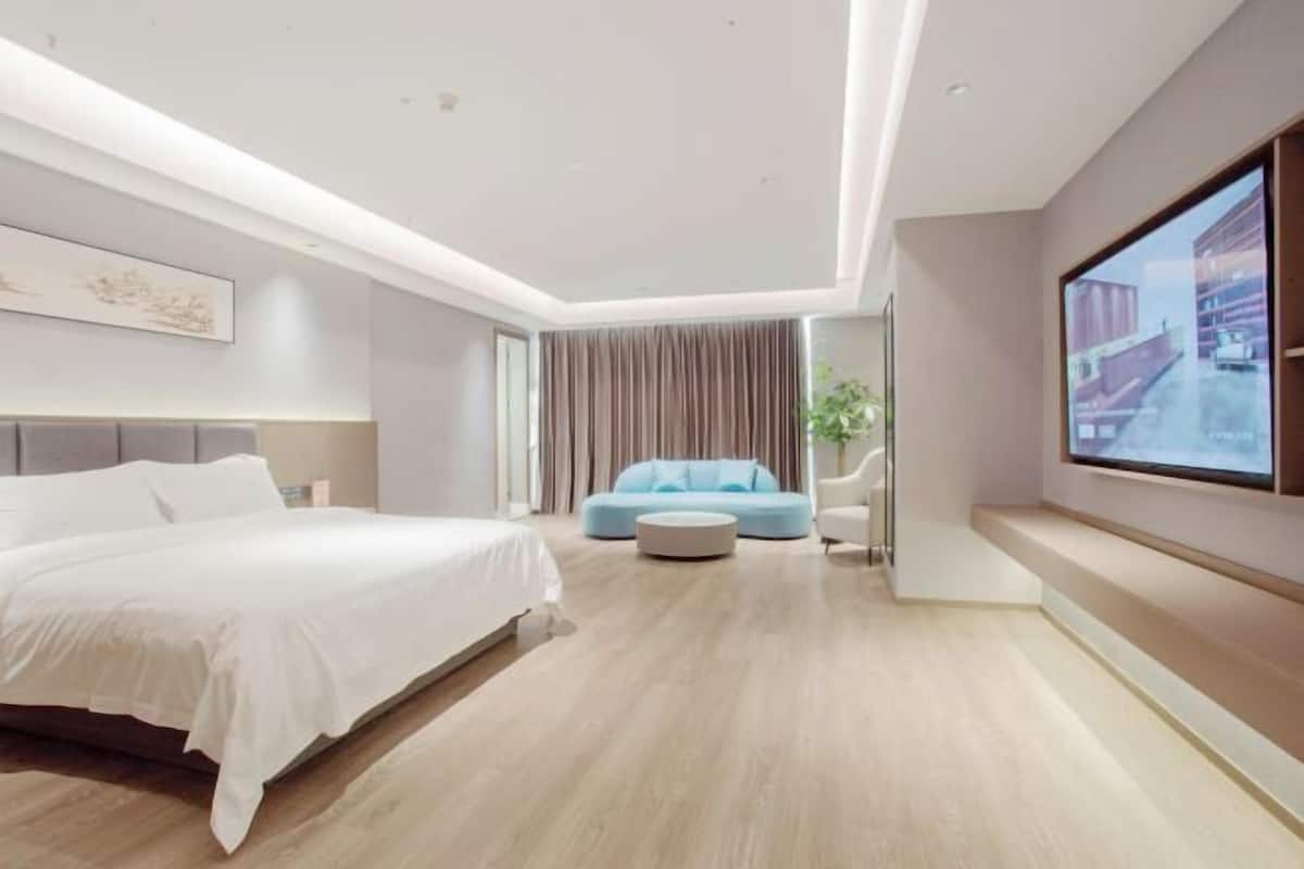 Un dormitorio moderno con una cama grande, un sofá azul, una mesa de centro redonda y un ventanal con vista a la ciudad.