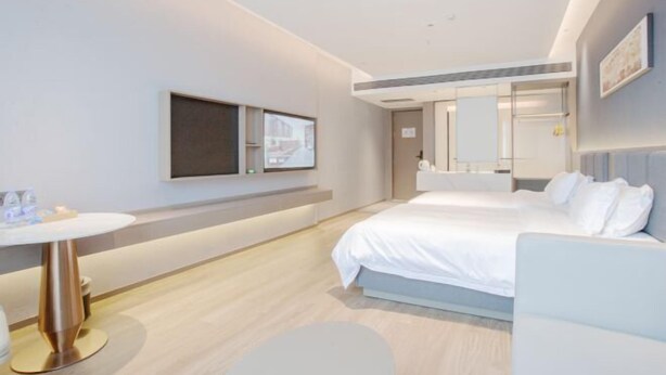 Una habitación de hotel moderna con una cama grande, una mesita de noche, un televisor montado en la pared y un pequeño rincón de descanso con una silla y una mesa.