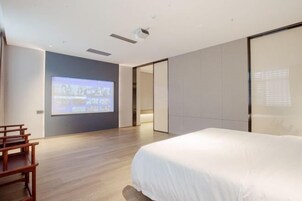 Una habitación de hotel moderna con una cama grande, una silla de madera, una pantalla de proyector y una puerta corredera.