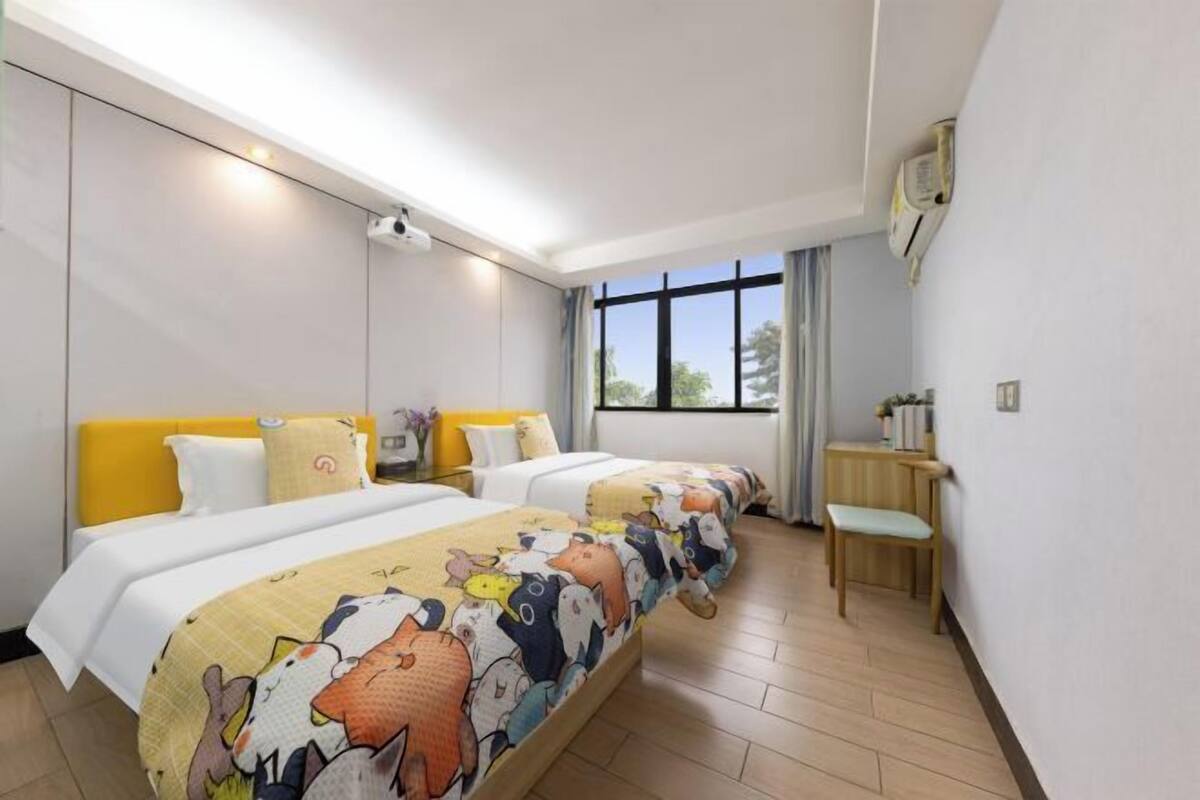 A hotel room with two beds, a desk, and a window with a view of trees.