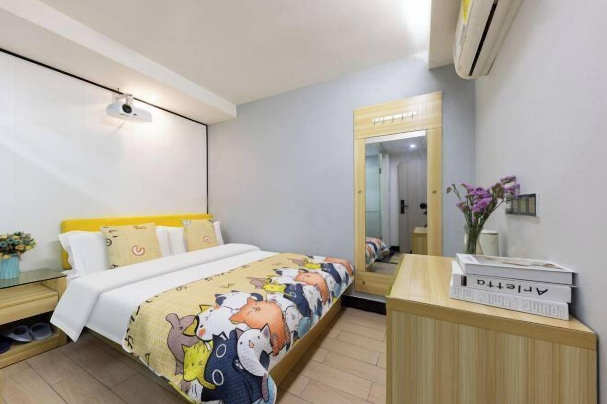 A hotel room with a bed, bedside table, and a mirror.
