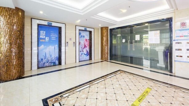 A modern hotel lobby with a clean, tiled floor, a glass elevator, and a large poster on the wall. - Shiman Art Hotel (Guangzhou Chebei Subway Station) (Guangzhou)