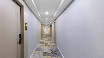 A hotel corridor with doors on both sides, a patterned carpet, and a ceiling with recessed lighting.