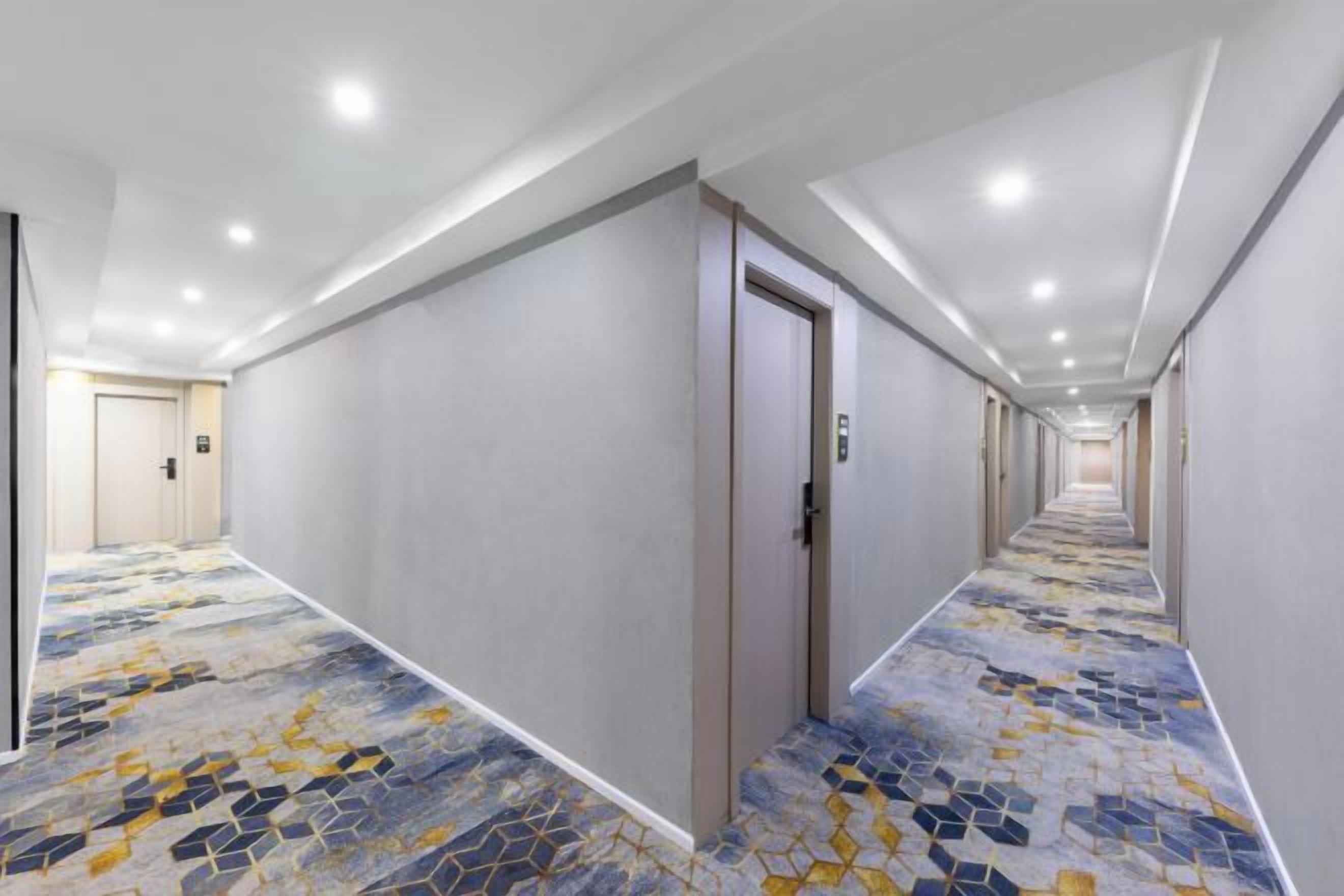 A hotel corridor with a patterned carpet, doors, and recessed lighting.