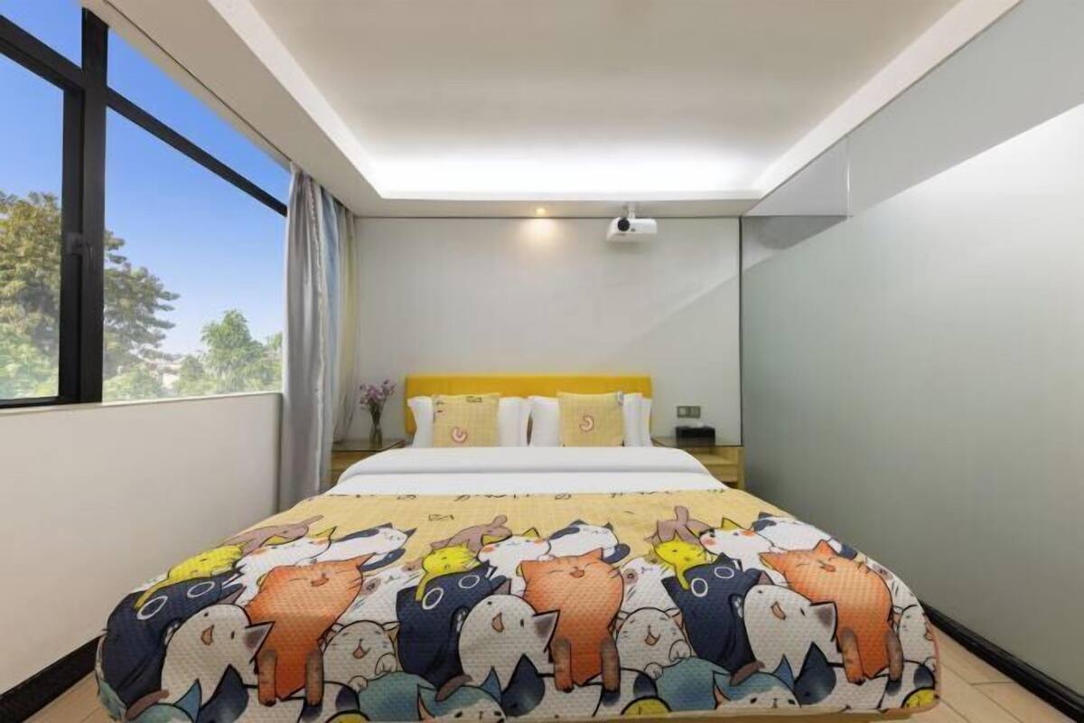 A bedroom with a large bed, a ceiling projector, and a window with curtains.