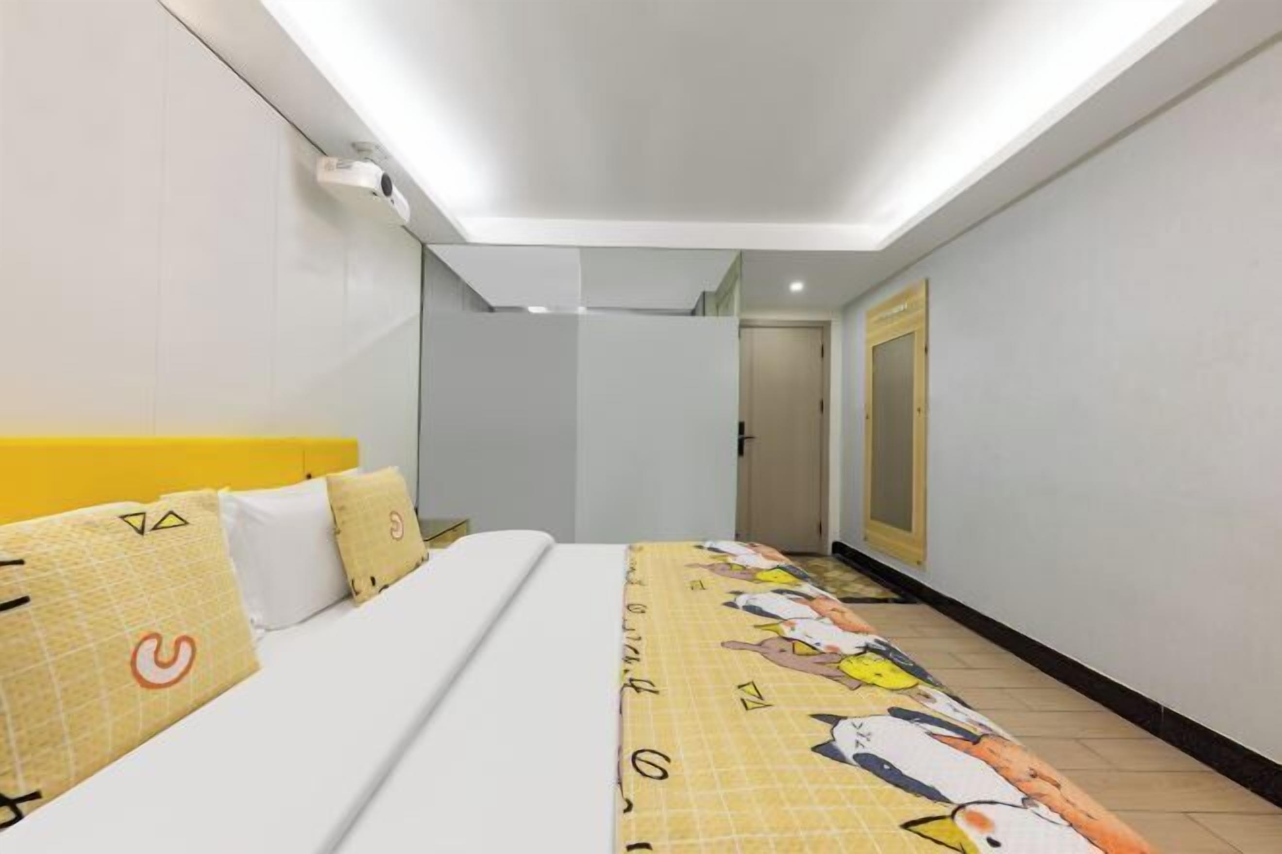 A hotel room with a bed, a headboard, a bedside table, a mirror, and a door.