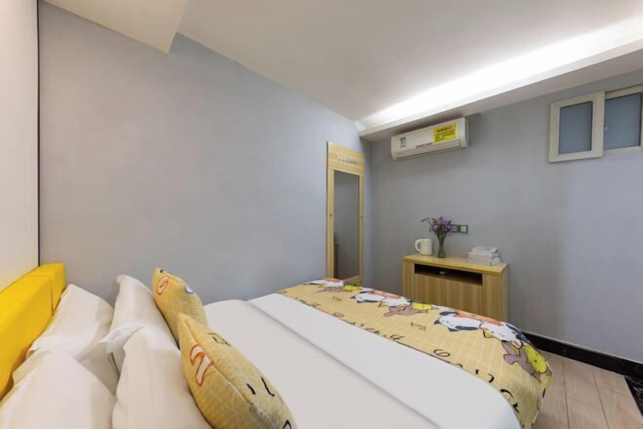 A bedroom with a bed, a bedside table, a mirror, and an air conditioning unit.